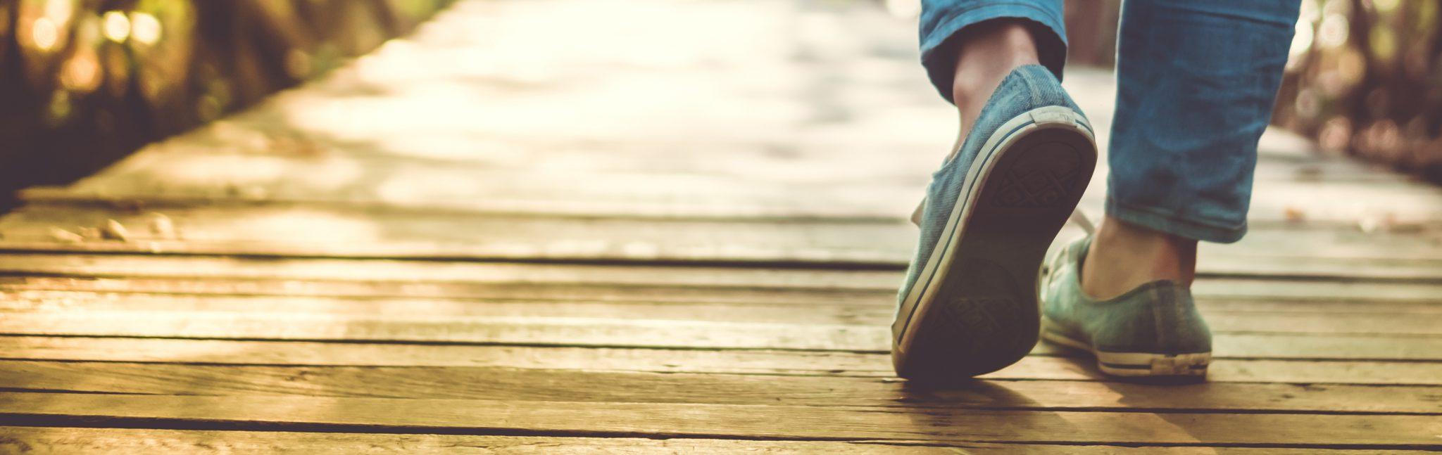 Person's feet on wood-decked trail with the rays of the low sun turning the wood grain flaxen.